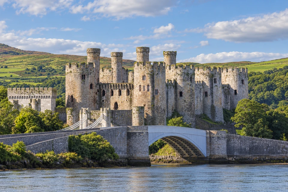 Conwy Castle's round stone towers and crenellated walls stand above the river bridges, with green Welsh hills behind.