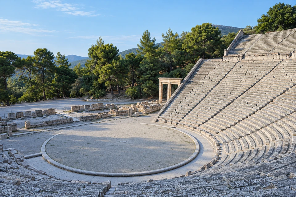 Ancient Epidaurus theatre with curved stone seating around its circular orchestra and wooded hills beyond.