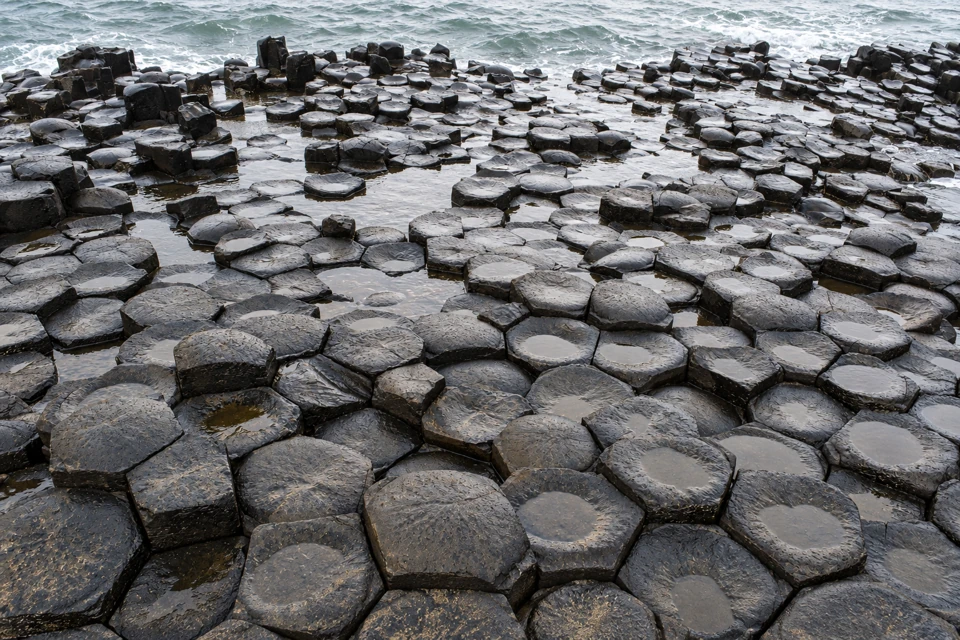 Dark interlocking polygonal basalt column tops with shallow pools of water meet the sea at the Giant's Causeway in Northern Ireland.