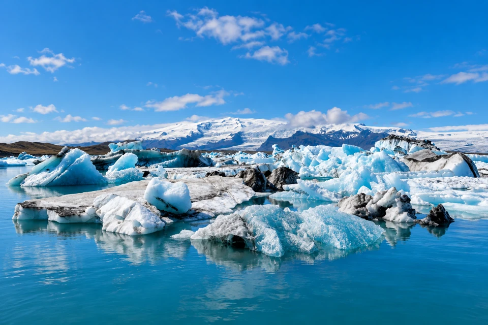 Blue-white icebergs with dark sediment streaks float on Jokulsarlon lagoon beneath the distant snow-covered glacier landscape.
