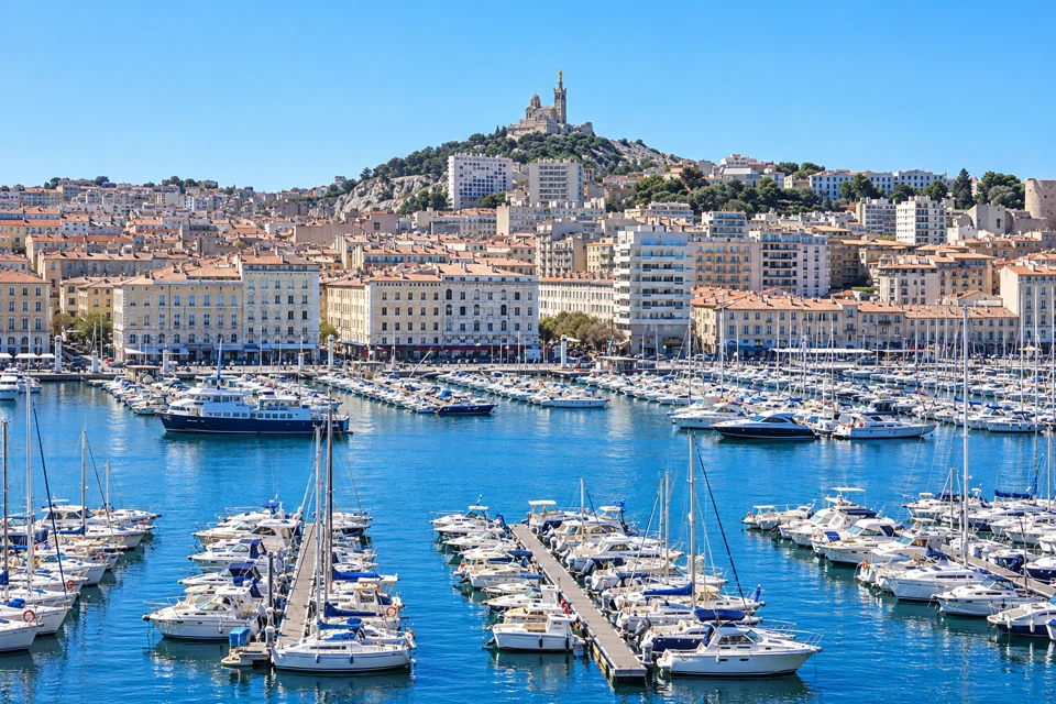 Marseille Vieux-Port marina with white boats, pale waterfront buildings and Notre-Dame de la Garde above the hillside.