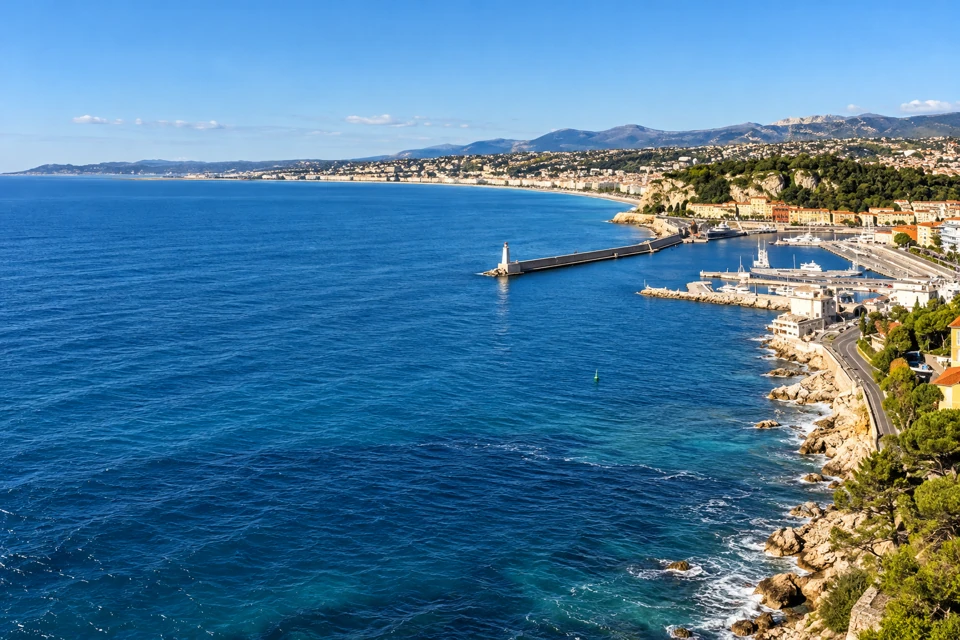The port of Nice and its breakwaters sit at right beside the blue Baie des Anges, with the city's curved coastline and low hills beyond.