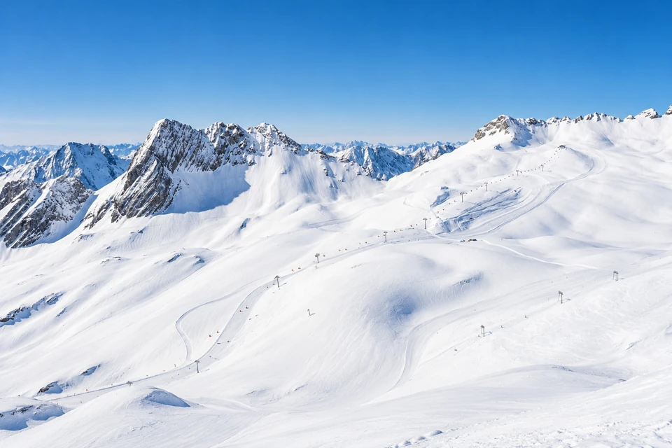Snow-covered Zugspitze plateau with marked ski slopes and rugged Wetterstein mountain ridges under a clear blue sky.